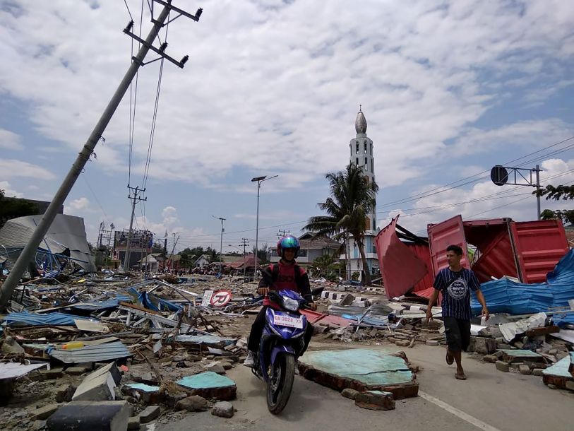 在印尼中苏拉威西省帕卢市,人们经过一处废墟