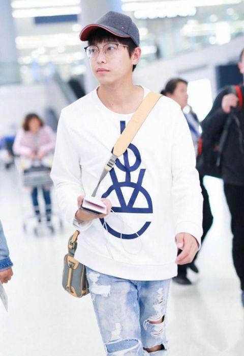 头戴灰色棒球帽，戴着眼镜斯文养眼，在机场边走边玩手机变“低头族”。