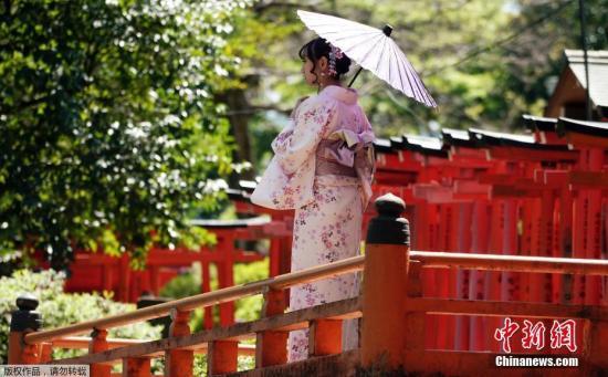 资料图：当地时间2019年4月16日，日本东京，一名身穿和服的女子在根津神社里拍照。