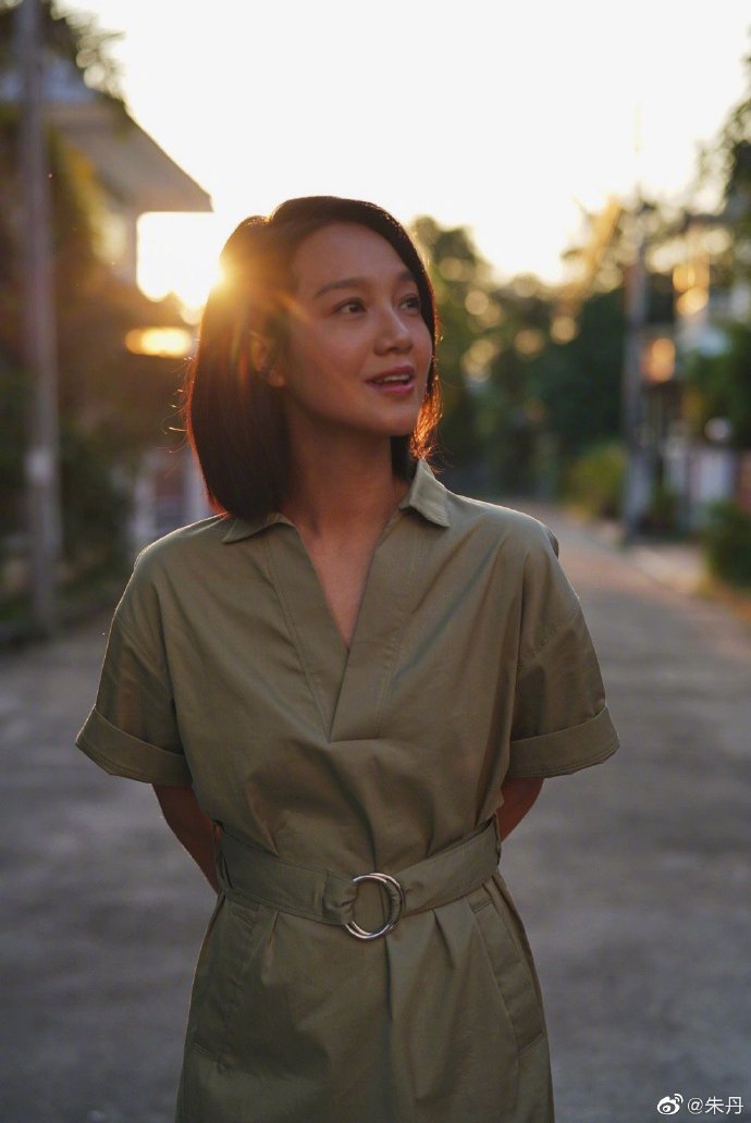 朱丹身穿军绿色连衣裙,背着双肩包举着相机,温柔地享受生活,在夕阳下