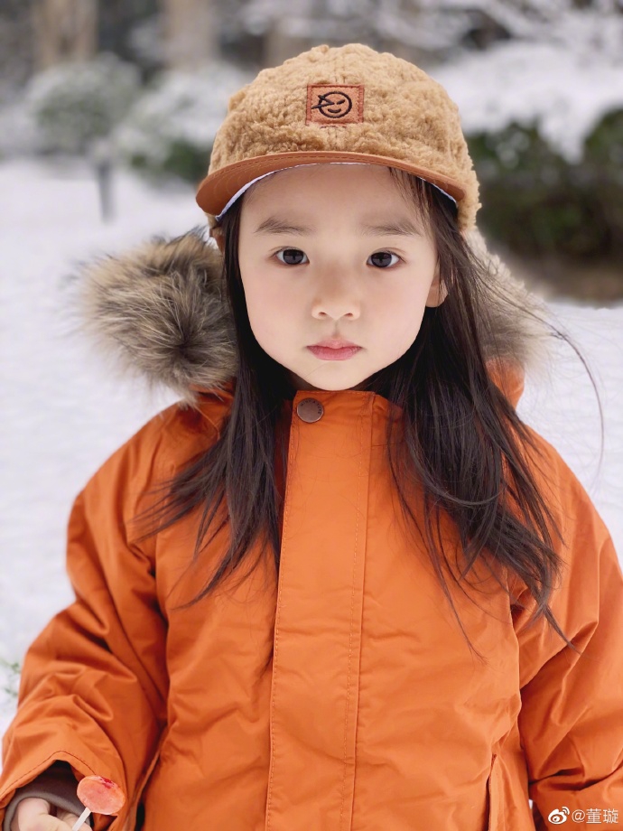 照片中的小酒窝头戴毛绒鸭舌帽,身穿橙色毛领外套和牛仔裤娇俏可爱