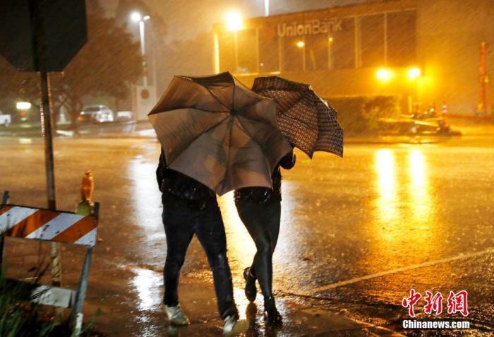 资料图：美国民众在狂风暴雨中前行。中新社记者 刘关关 摄