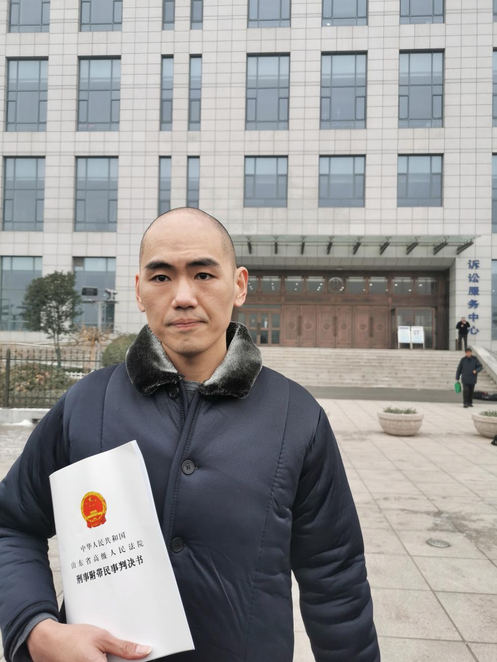 张志超手持判决书在淄博中院门前留影。 澎湃新闻记者 张家然 图