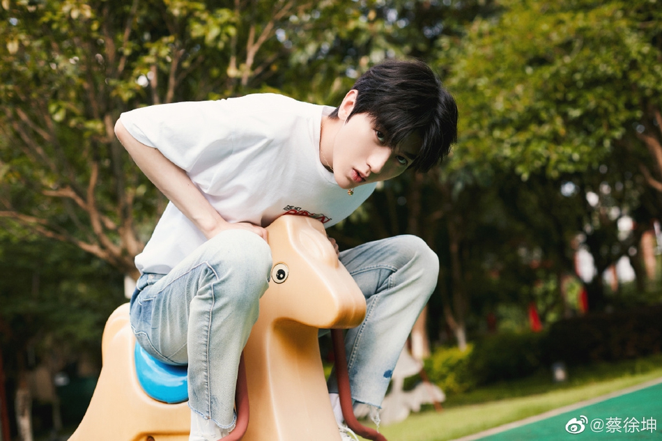 蔡徐坤穿白t搭牛仔裤清爽帅气 游乐场坐木马玩耍显童趣